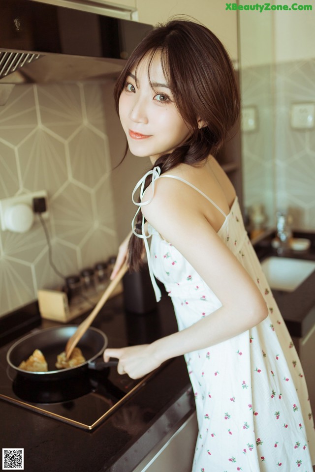 A woman in a white dress cooking food in a pan.