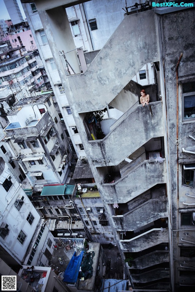 A woman is sitting on the balcony of an apartment building.