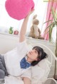 A woman laying on a bed holding a pink heart shaped pillow.