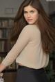 A woman with long brown hair standing in front of a bookshelf.