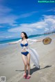 A woman in a blue bikini and a straw hat on the beach.