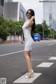 A woman in a white dress is standing on the street.