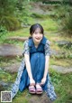 A woman in a blue dress sitting on a rock in the grass.