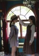 Two young women standing next to each other in front of a window.