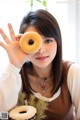 A woman holding a donut in front of her face.