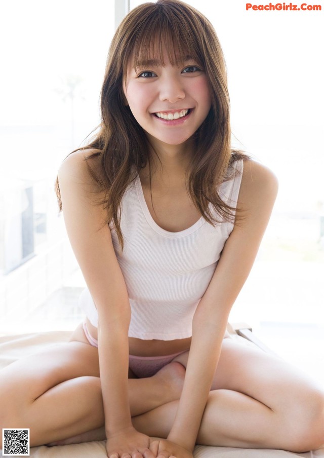 A young woman sitting on a bed smiling at the camera.