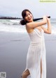 A woman in a white dress holding a baseball bat on the beach.